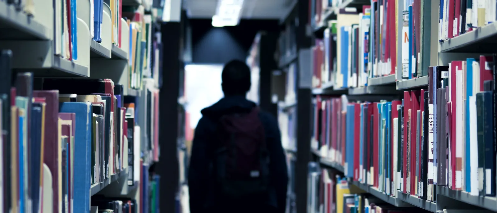 Estudante caminhando entre as estantes de uma biblioteca